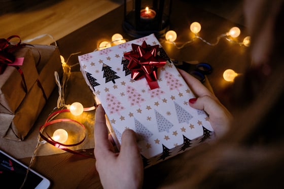 person-holding-gift-box-with-red-ribbon-beside-string-lights-1687049